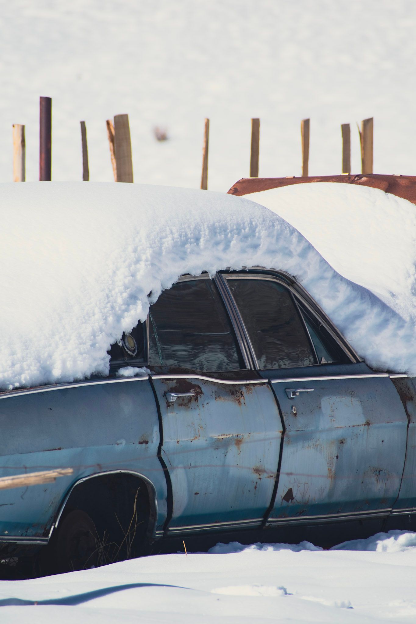 Auto viejo celeste y oxidado con el techo cubierto por una capa gruesa de nieve