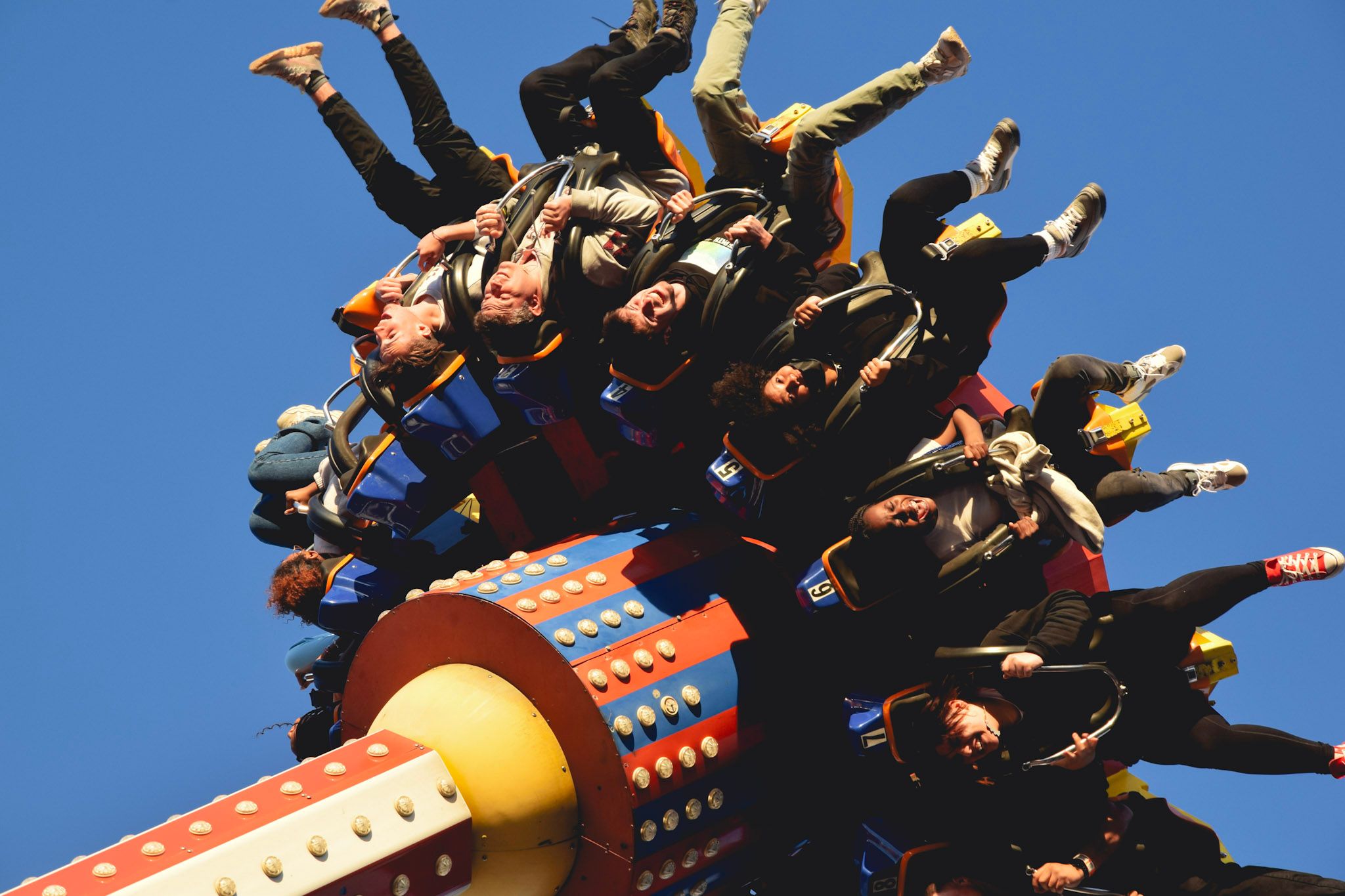 Personas gritando cabeza abajo en un juego mecánico de un parque de diversiones, contra el cielo azul