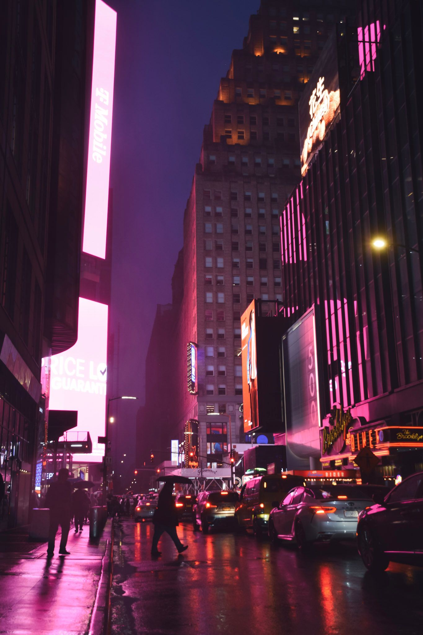 Calle mojada iluminada por carteles rosados y violetas, con gente cruzando y autos en la niebla