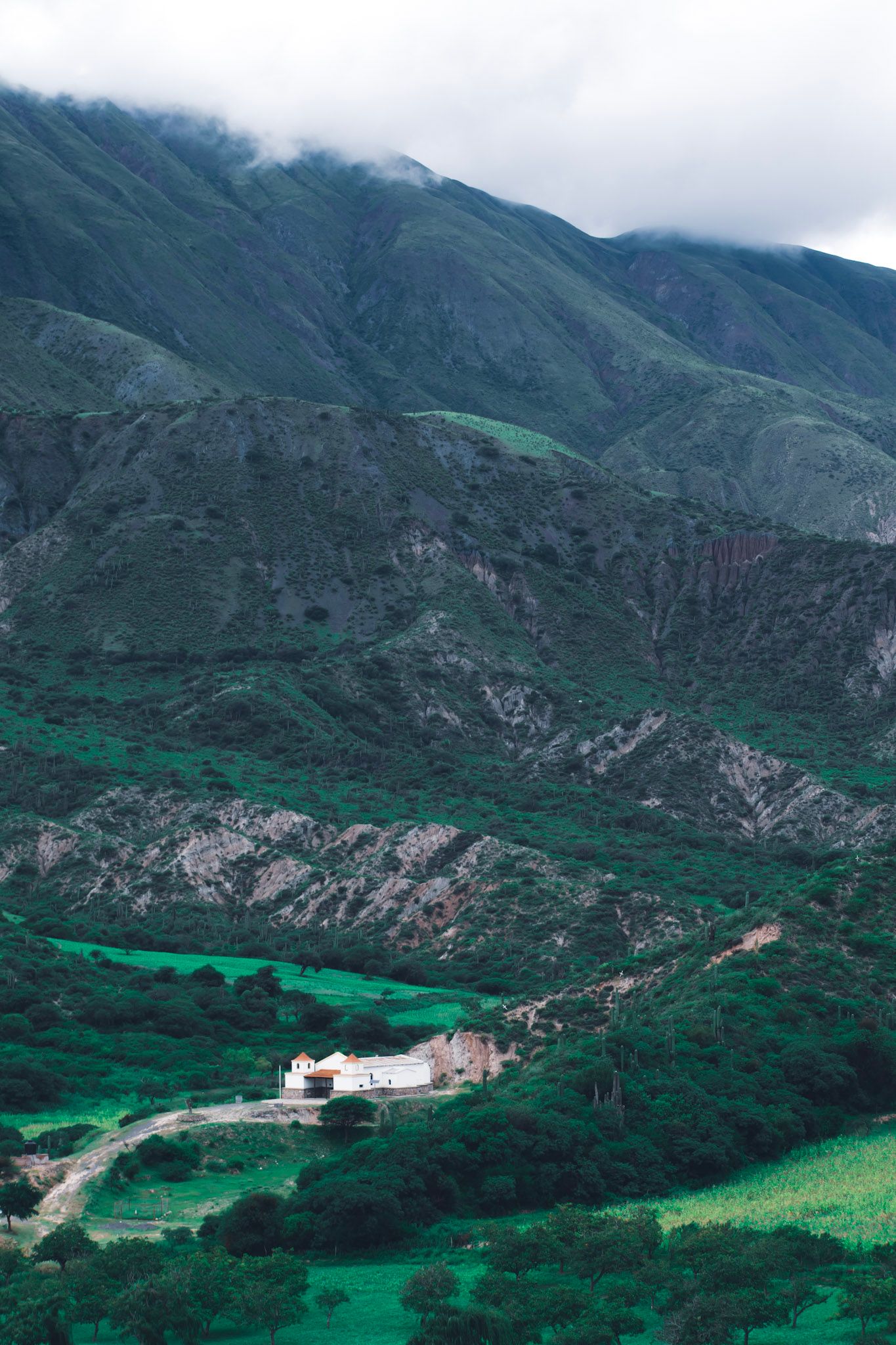 Casa blanca pequeña en un valle verde al pie de montañas con nubes bajas