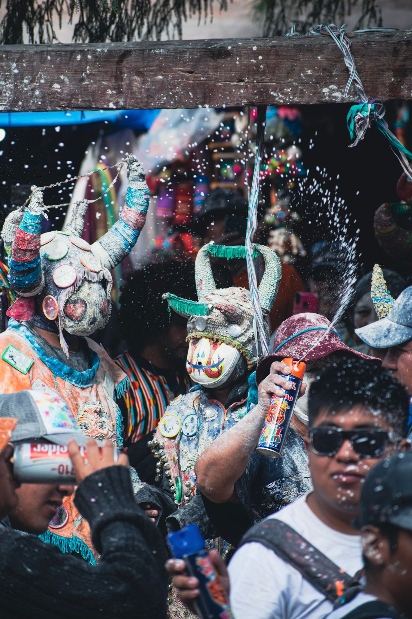 Diablos de carnaval con máscaras de cuernos y trajes de espejitos entre la gente, bajo una lluvia de espuma