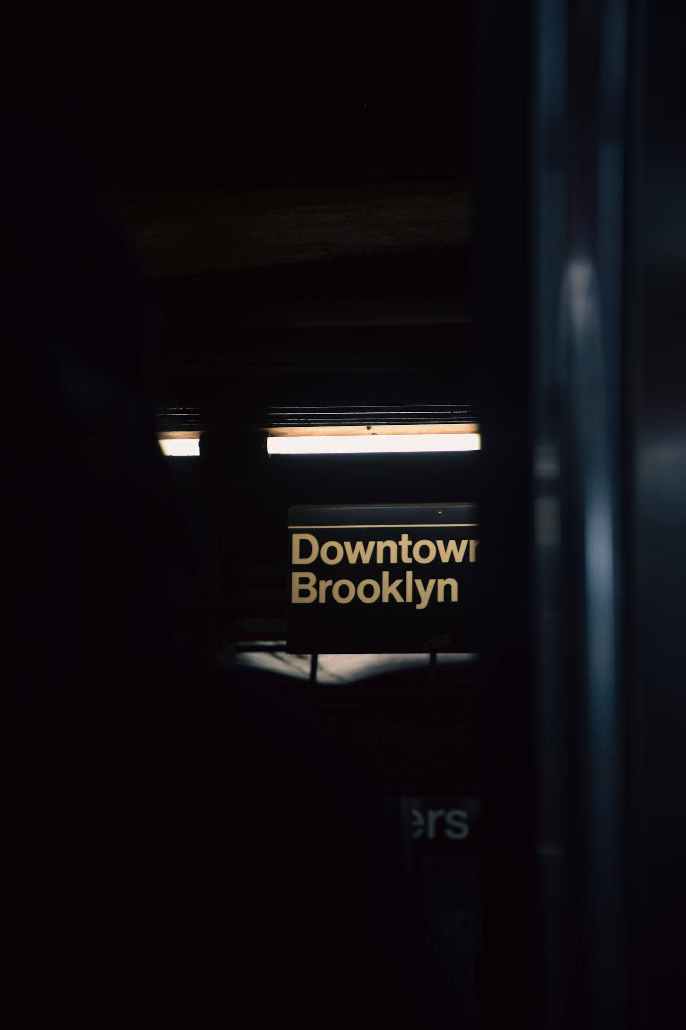 Cartel iluminado de Downtown Brooklyn en un andén del subte, visto en la penumbra desde dentro de un vagón