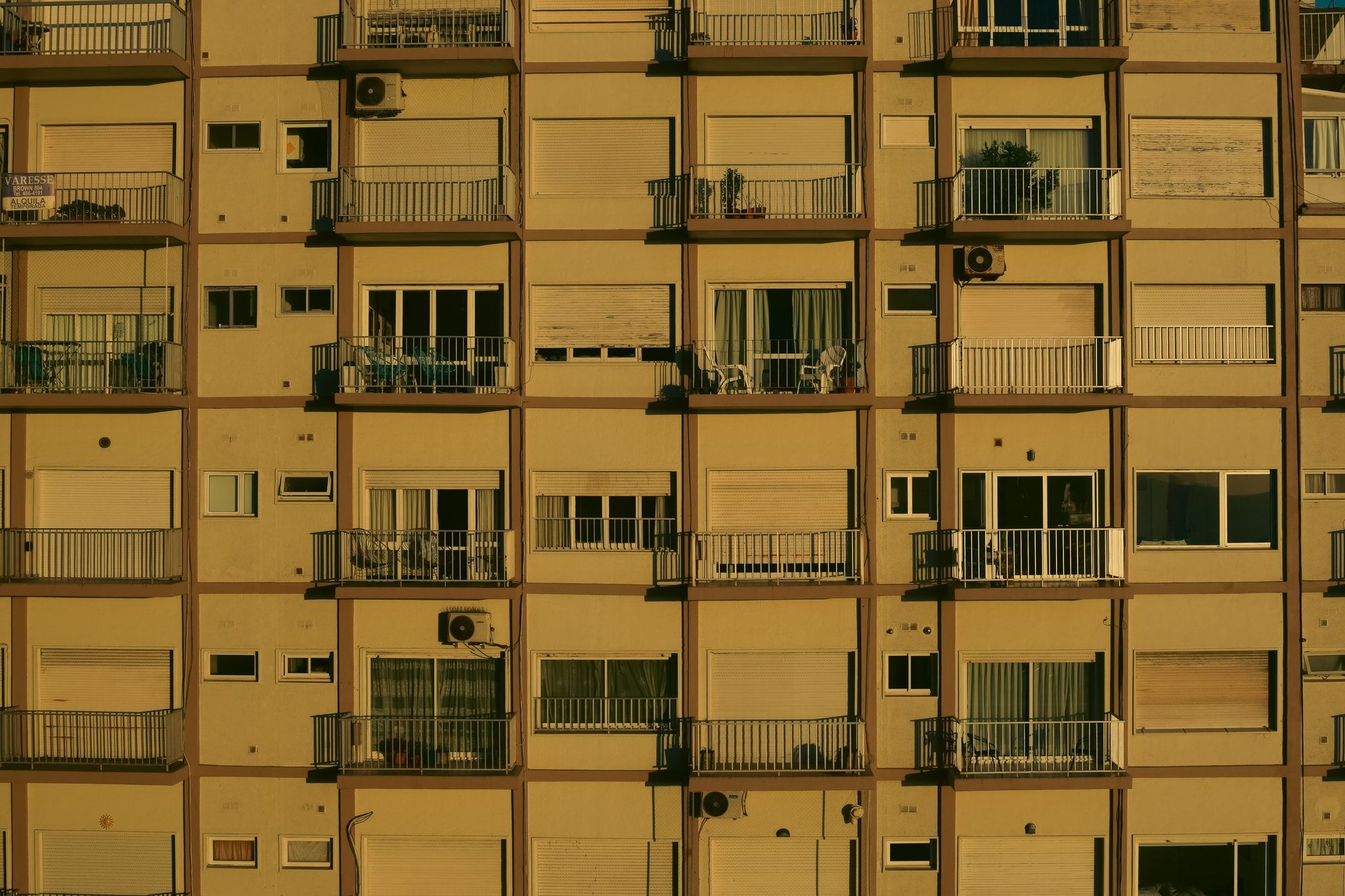 Fachada de un edificio de departamentos con balcones, iluminada por una luz cálida amarilla