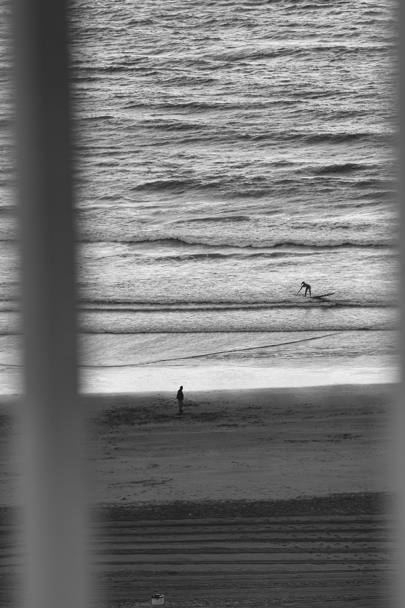 La orilla del mar con una persona caminando, vista entre cortinas, en blanco y negro