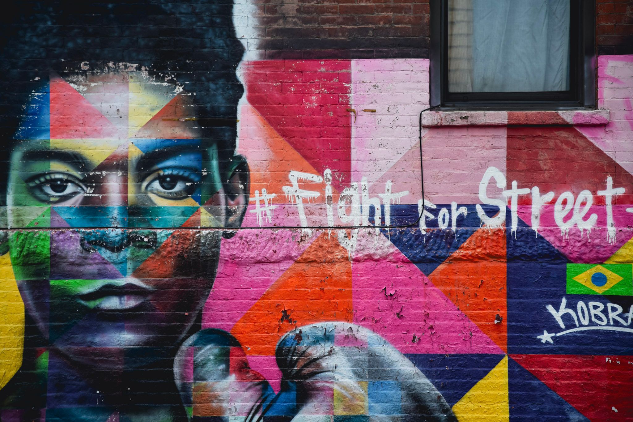 Mural de un rostro pintado con triángulos de colores y la frase Fight for Street Art sobre una pared de ladrillo