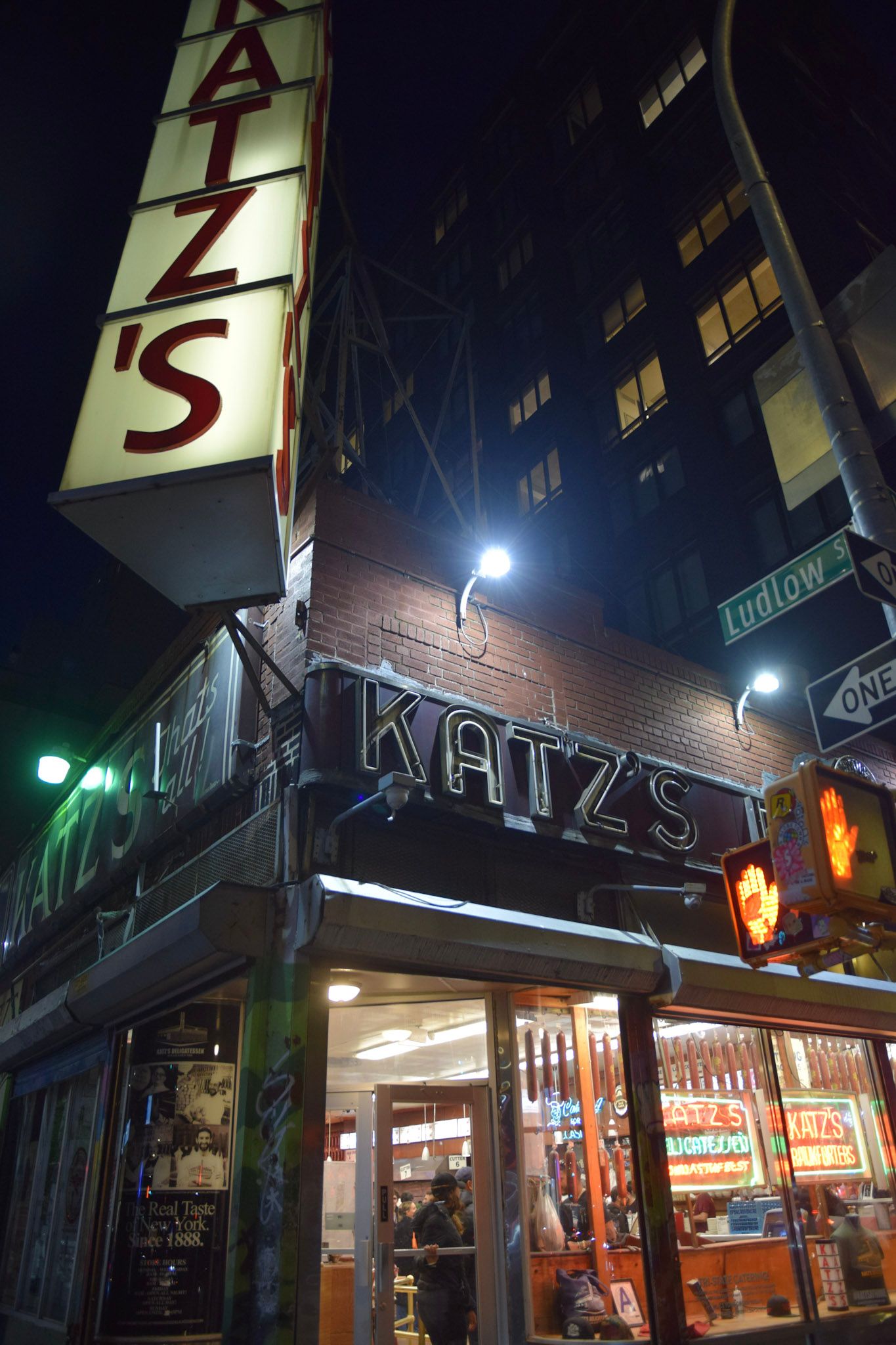La esquina de Katz's Delicatessen de noche, con el cartel vertical iluminado y la vidriera llena de neones