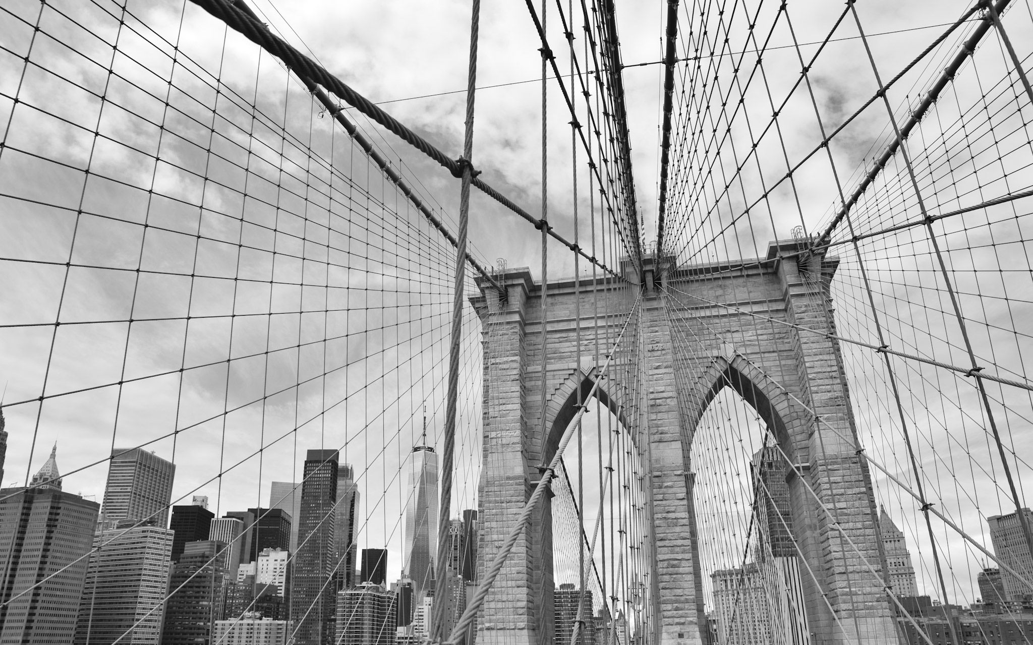 La red de cables del puente de Brooklyn convergiendo hacia la torre de piedra con arcos góticos, en blanco y negro