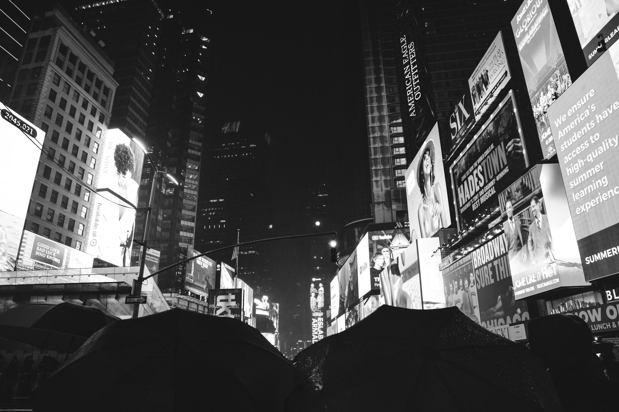 Times Square bajo la lluvia, con pantallas gigantes y paraguas en primer plano, en blanco y negro