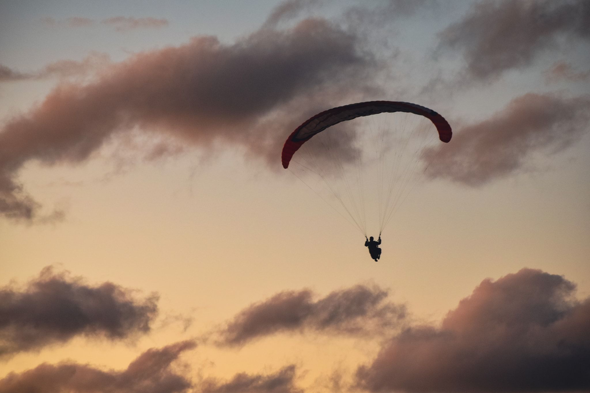 Parapente en vuelo recortado contra nubes rosadas del atardecer