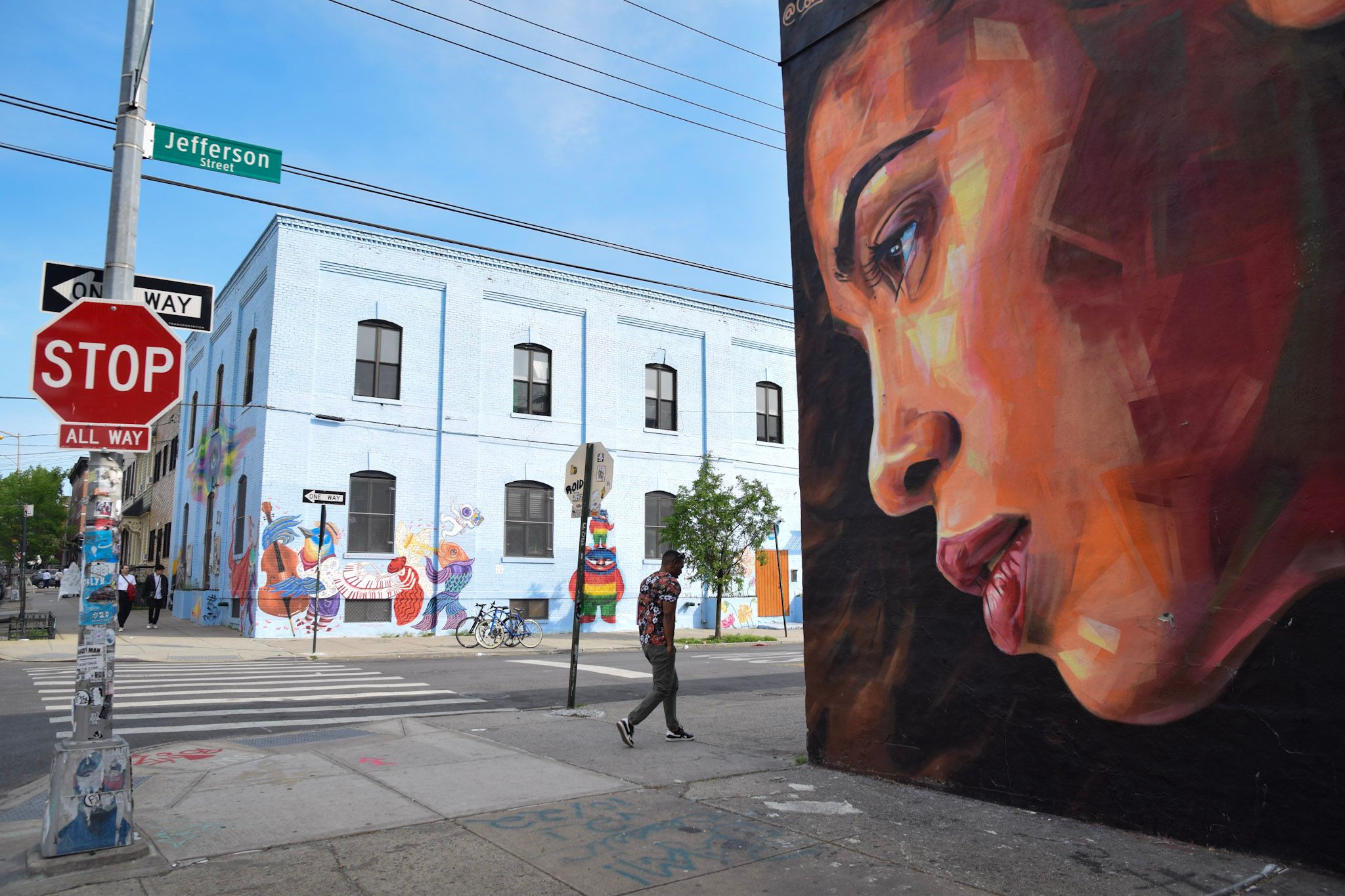 Mural gigante del perfil de una mujer en una esquina, con un cartel de PARE y un hombre cruzando la calle
