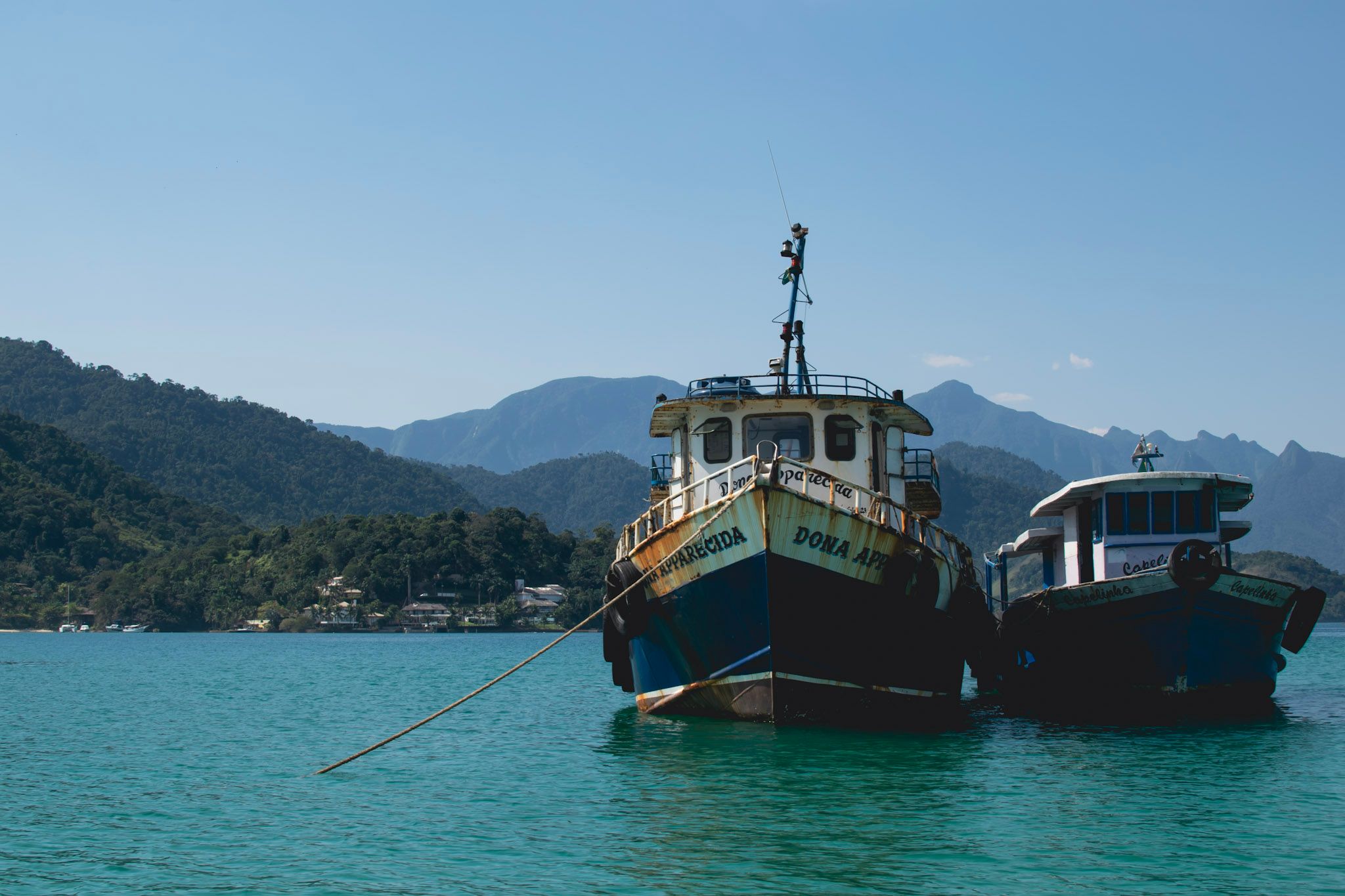 Dos barcos pesqueros anclados en agua verde, con cerros cubiertos de selva de fondo