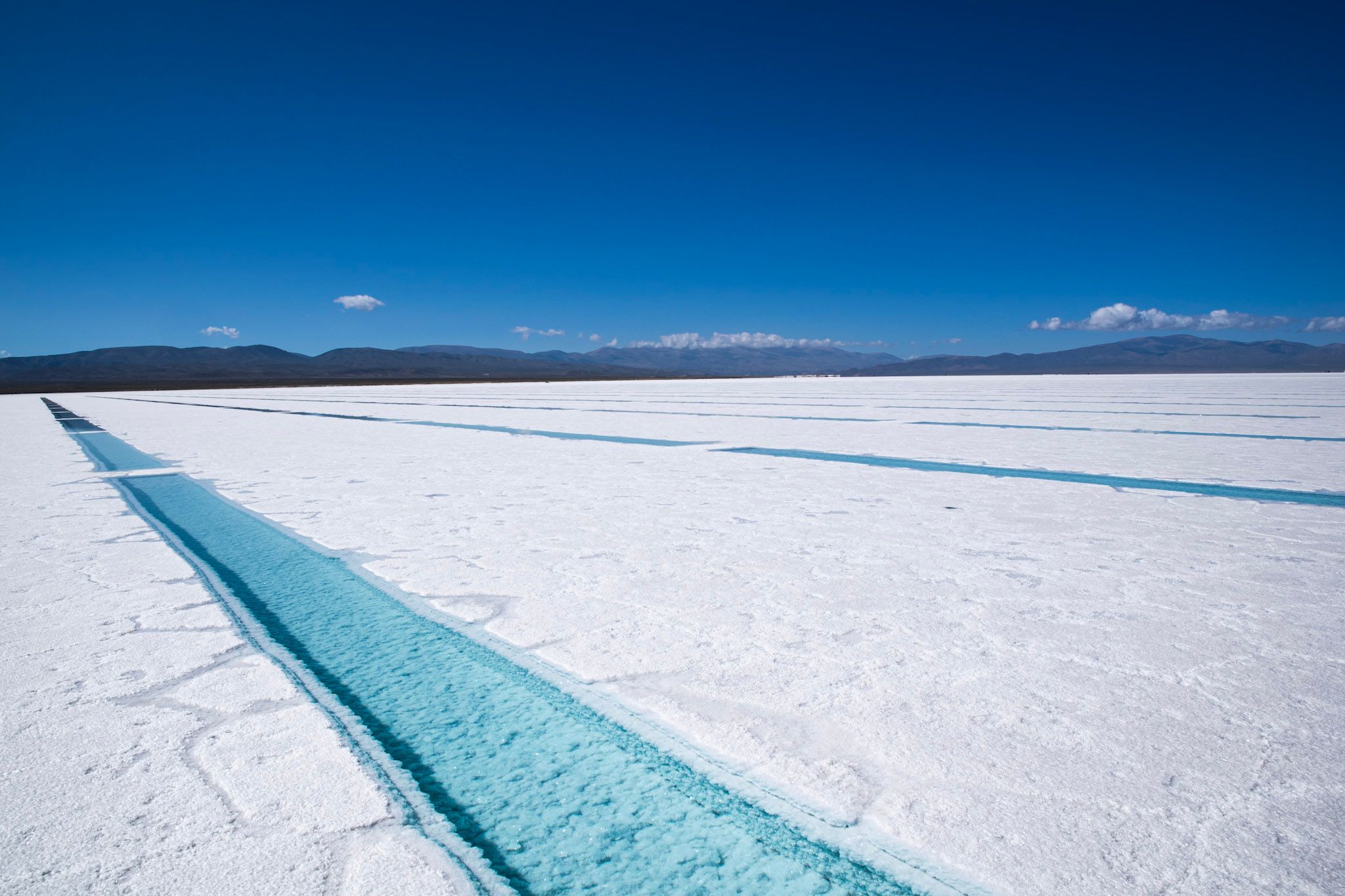 Salina blanca hasta el horizonte cruzada por un canal de agua celeste bajo un cielo azul profundo