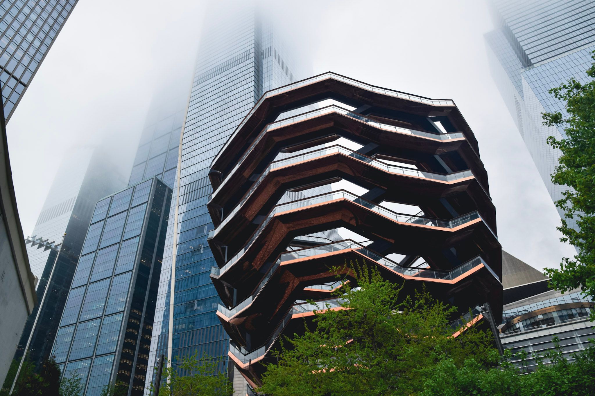 La estructura en panal del Vessel en Hudson Yards, con rascacielos de vidrio que se pierden en la niebla y árboles verdes al pie